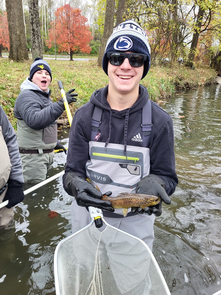 boy holding fish he caught with net he is also holding; smiling with sunglasses on in water wearing beanie