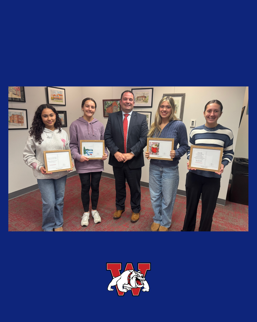 Five people stand indoors, smiling for a photo. Four students hold framed certificates or artwork, standing on either side of an adult in a suit and red tie. Framed artwork hangs on the wall behind them, and a blue border with a “W” bulldog logo appears at the bottom of the image.