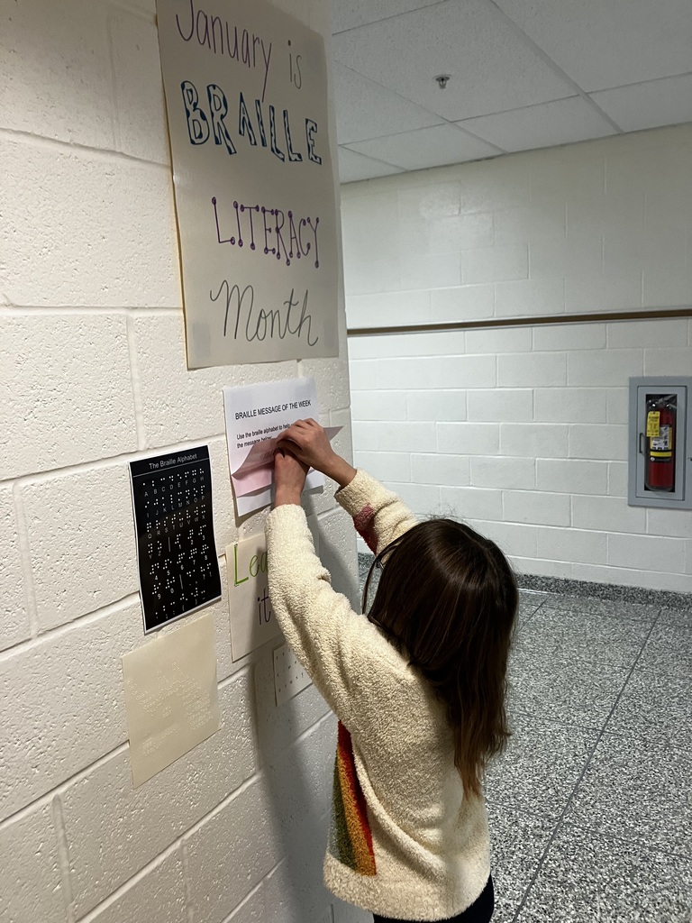 student is reaching up and reading braille message on the wall
