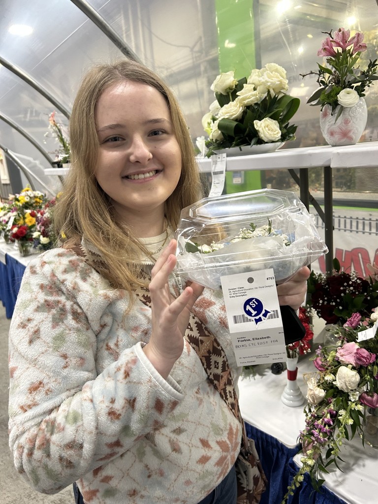 Girl holding a flower in a container that has a first place ribbon attached 