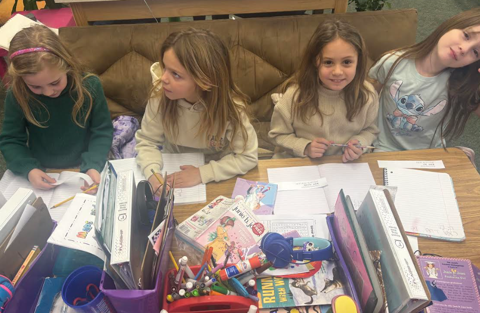 Two girls sitting at table learning how to write in chinese