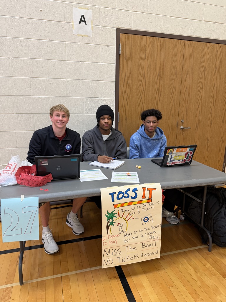 Three boys at table with sign for Toss it game