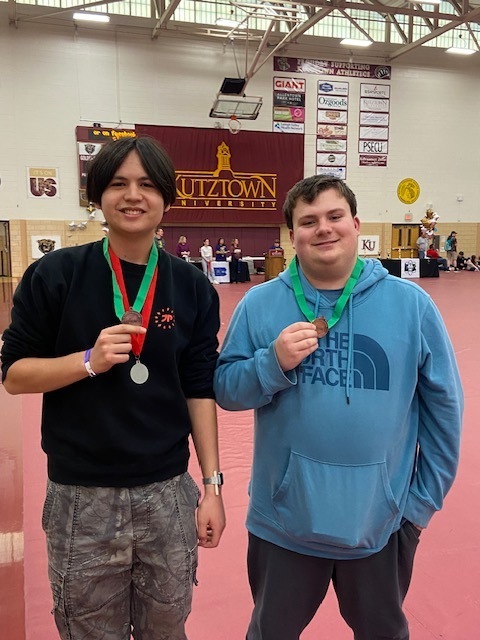 two students standing next to eachother holding medals