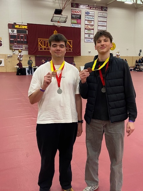 two students standing next to eachother holding medals