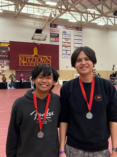 two students standing next to eachother holding medals