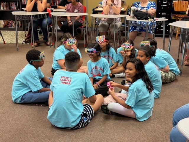 students in blue shirts sitting in circle on the floor