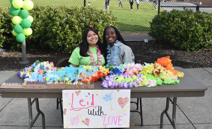 two girls sitting at table with a sign saying leid with love and leis on the table