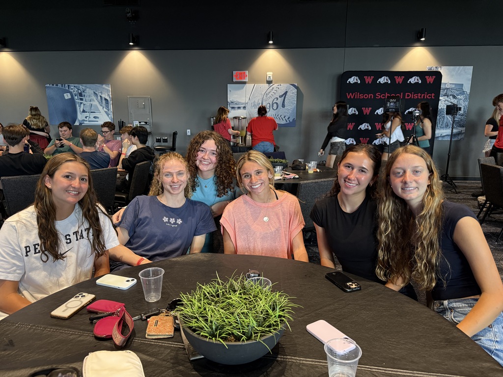 students sitting at table smiling at camera inside