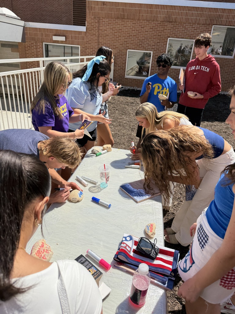 students decorating rocks at table outside