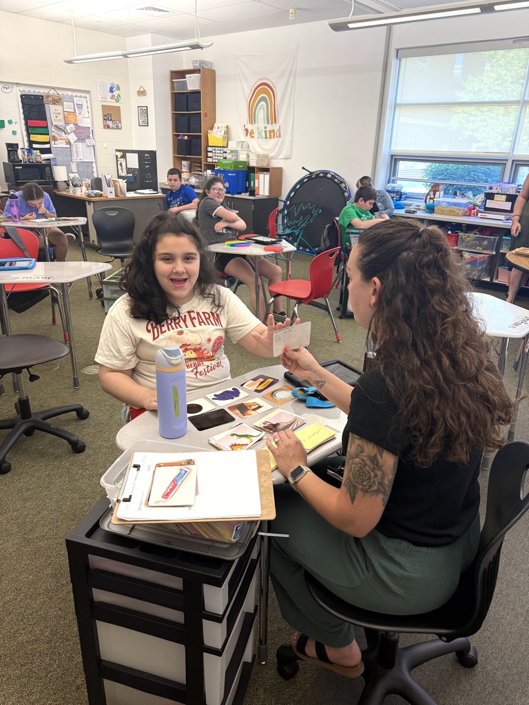 students smiling at camera while teacher shows card