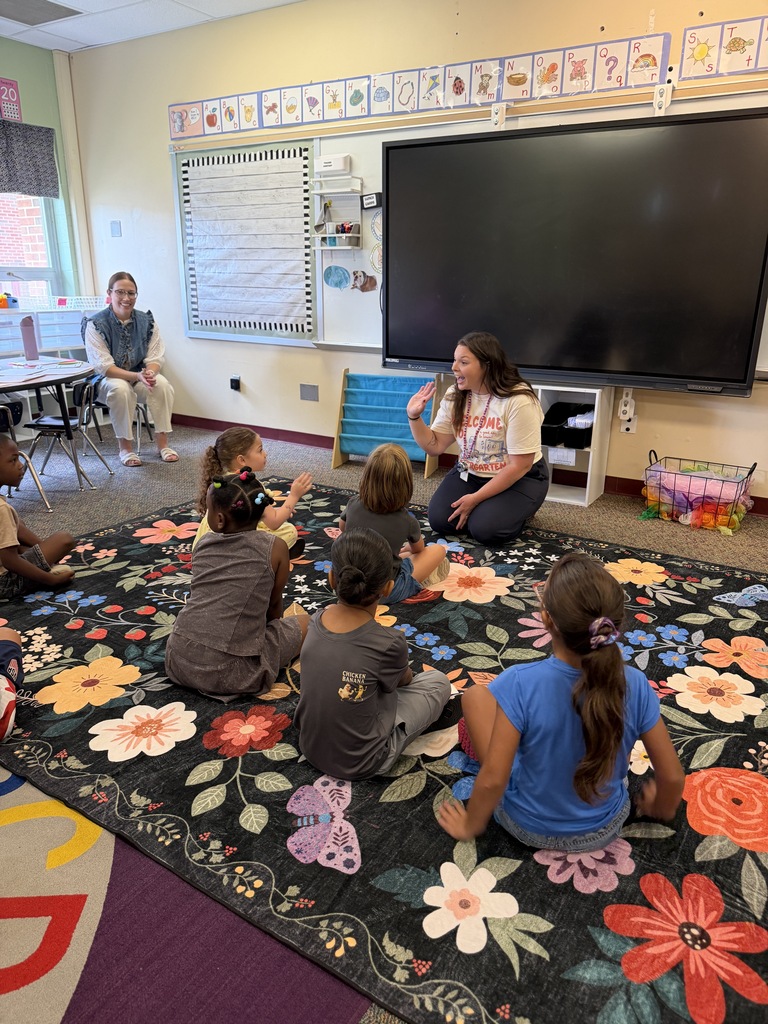 teacher waving at students on the carpet