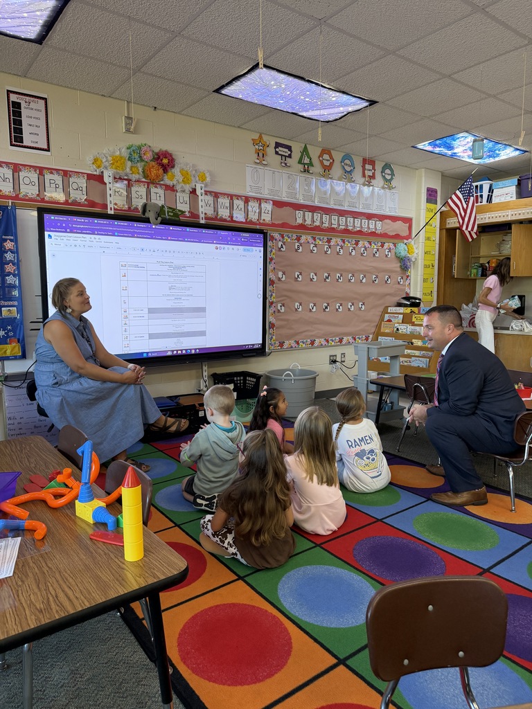 students sitting on the carpet next to superintendent