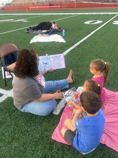 students reading book on field with teacher