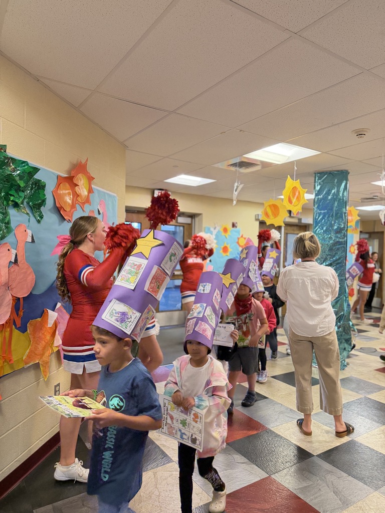 students wearing reader caps walking through cheerleaders