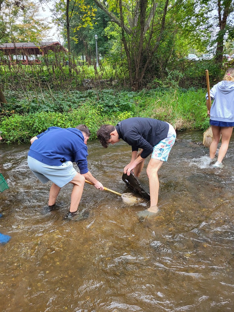 students in creek with a shovel