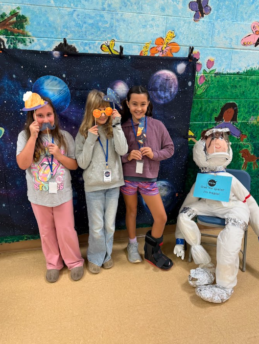 students holding masks up to face standing in front of space backdrop