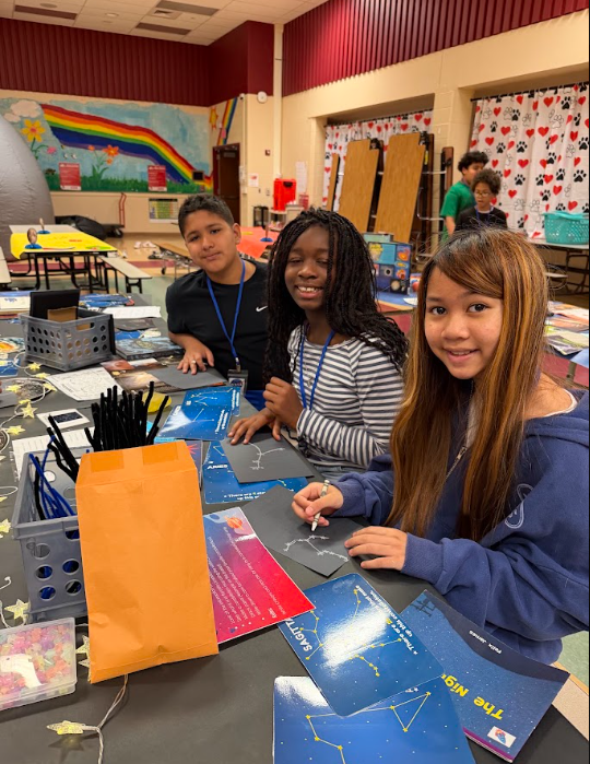 students sitting at cafeteria table smiling at the camera while working with notecards that have stars on them