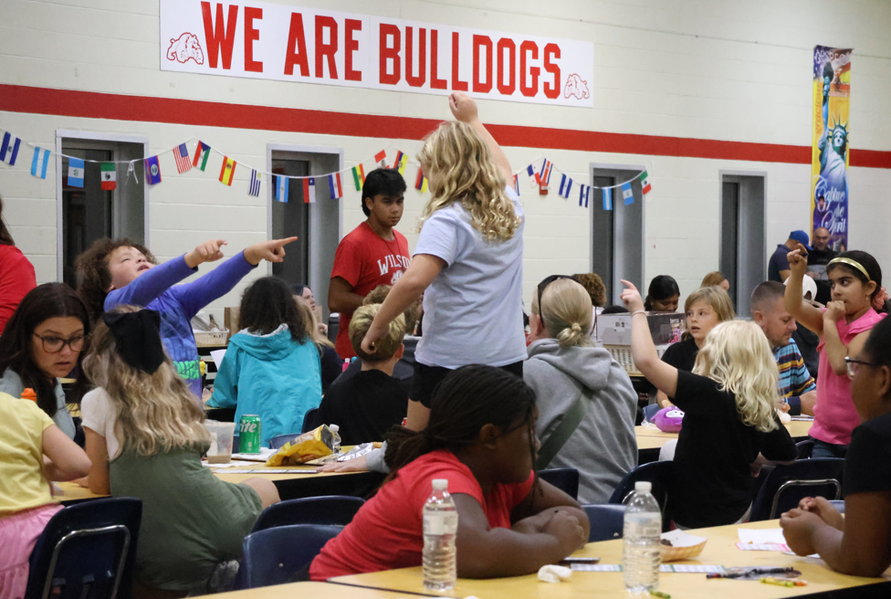 child standing up on chair after winning bingo with others around pointing