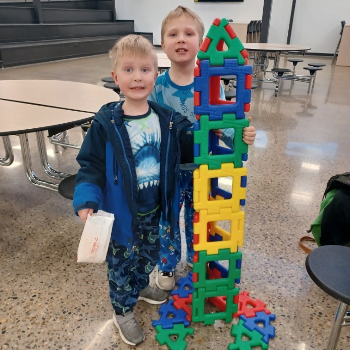 Two boys standing by a block tower.