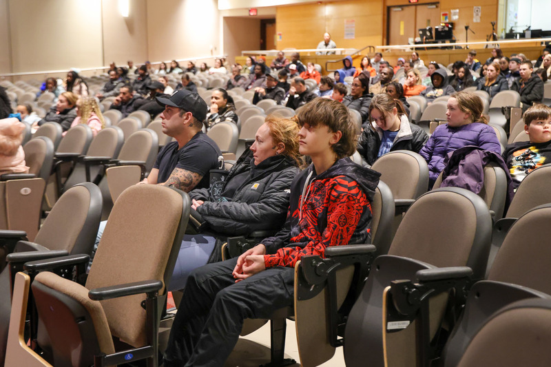 A family is listening to a presentation in an auditorium full of families
