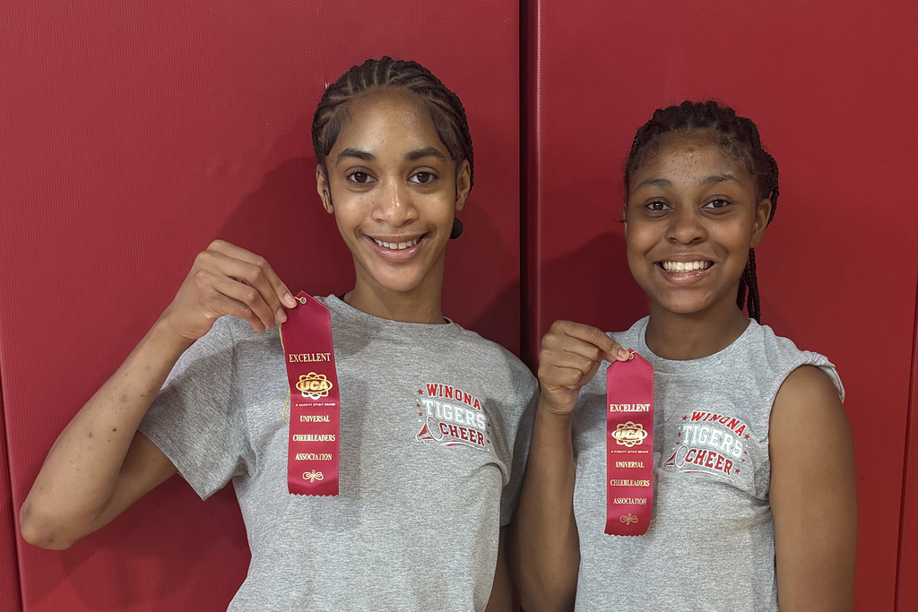 Two girls hold red ribbons and pose together, standing in front of a red wall.