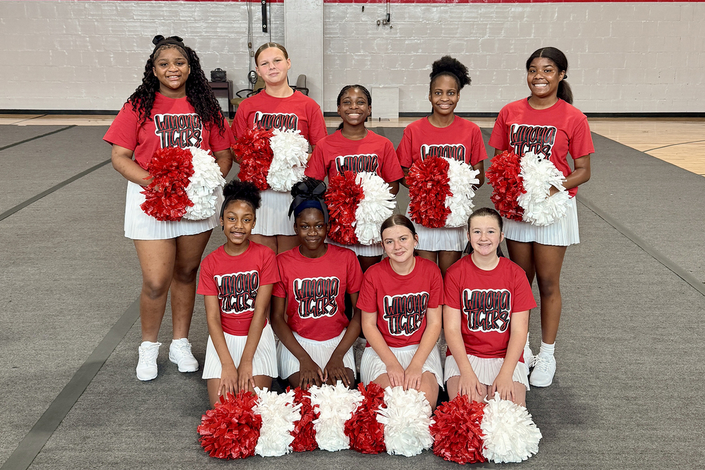 A group of cheerleaders in red and white uniforms pose in a gym with red and white pom-poms.