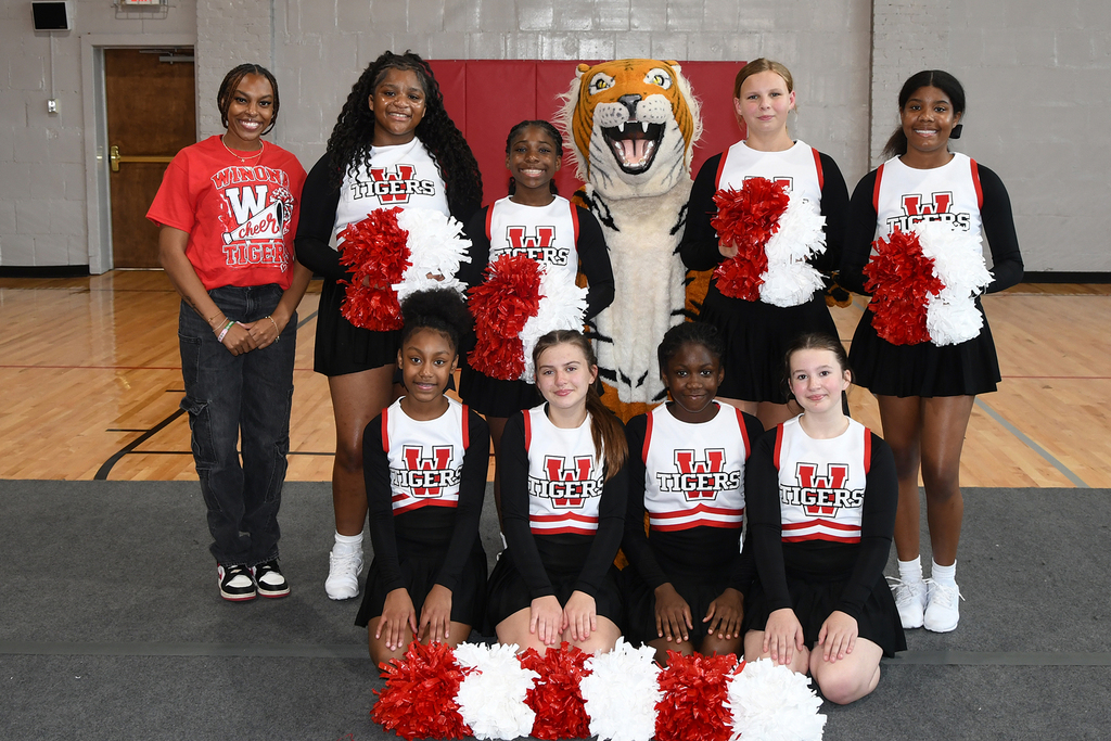 A cheerleading team poses for a photo with their mascot, a tiger, in a gymnasium.