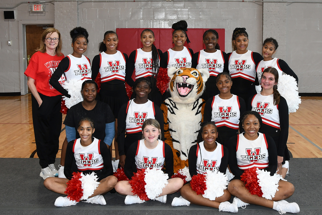 Group of cheerleaders in matching uniforms with a mascot in the center, in a gymnasium.