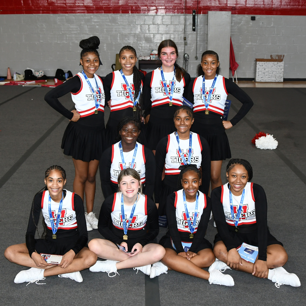 Group of young women, some in black dresses, all wearing medals, sitting and standing in rows.
