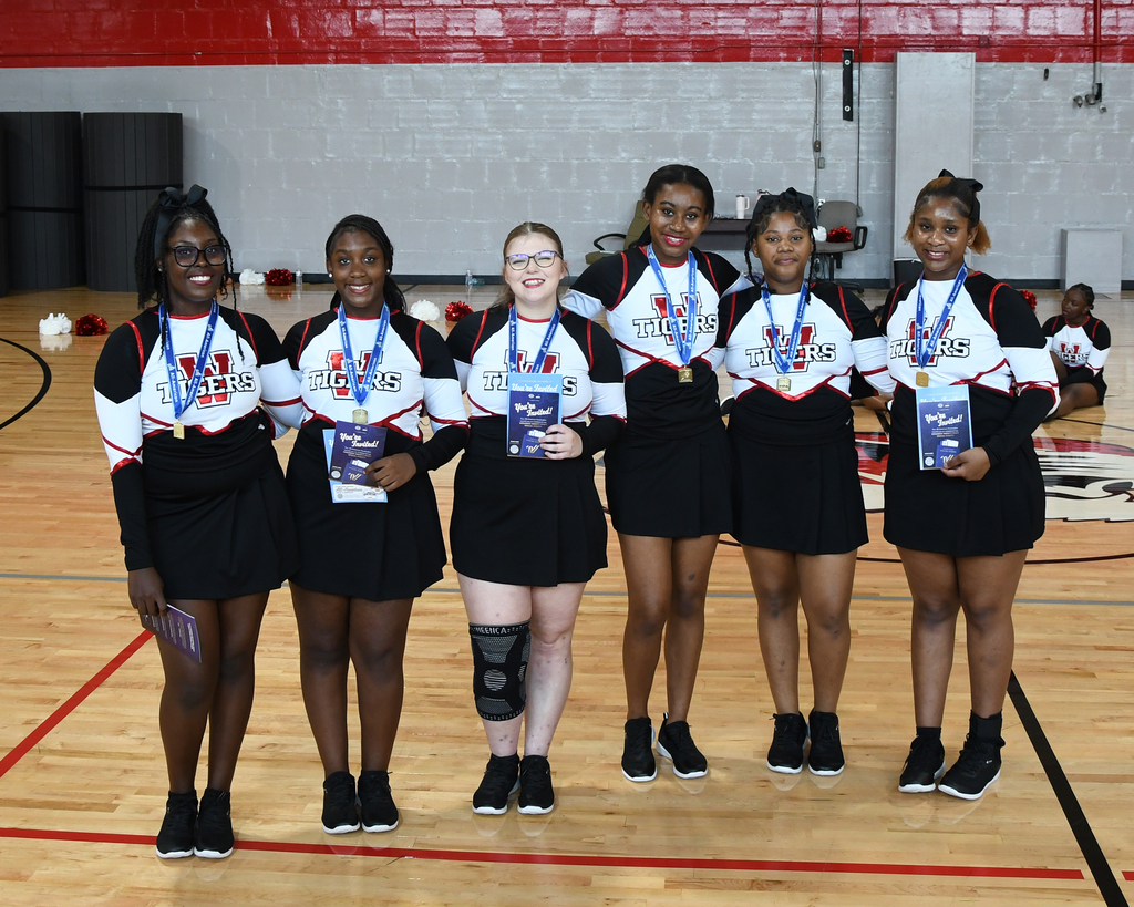 Seven women in matching uniforms stand in a row on a basketball court. They hold awards.