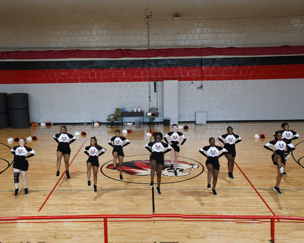 Team of female athletes in black and white uniforms practicing a routine on a basketball court.