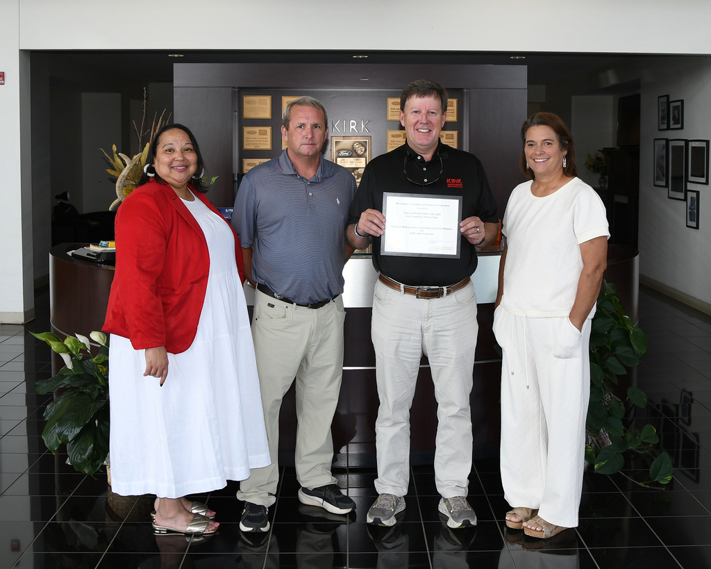 A group of four people standing in a room holding a certificate. Two women and two men.