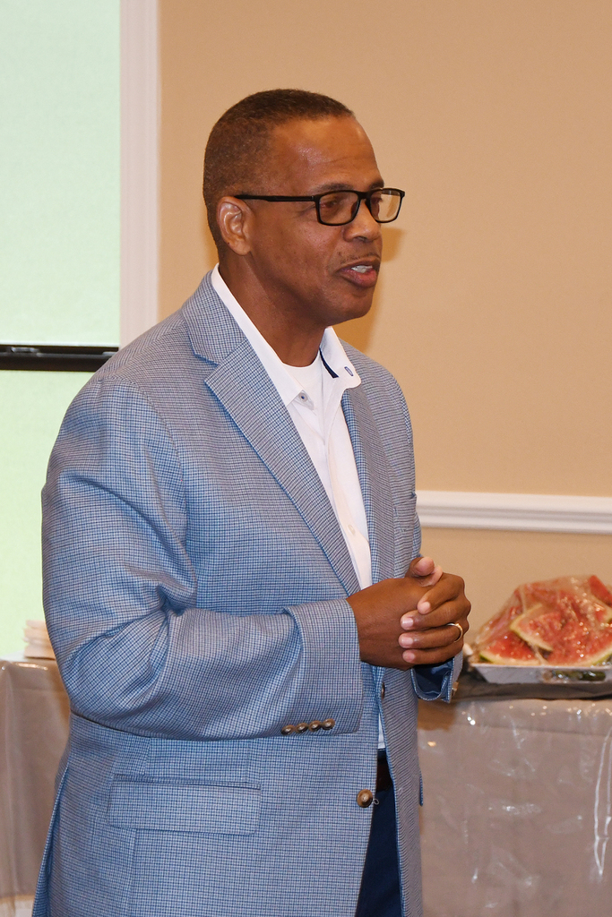 A man in a blue suit and glasses standing in front of a table with food.