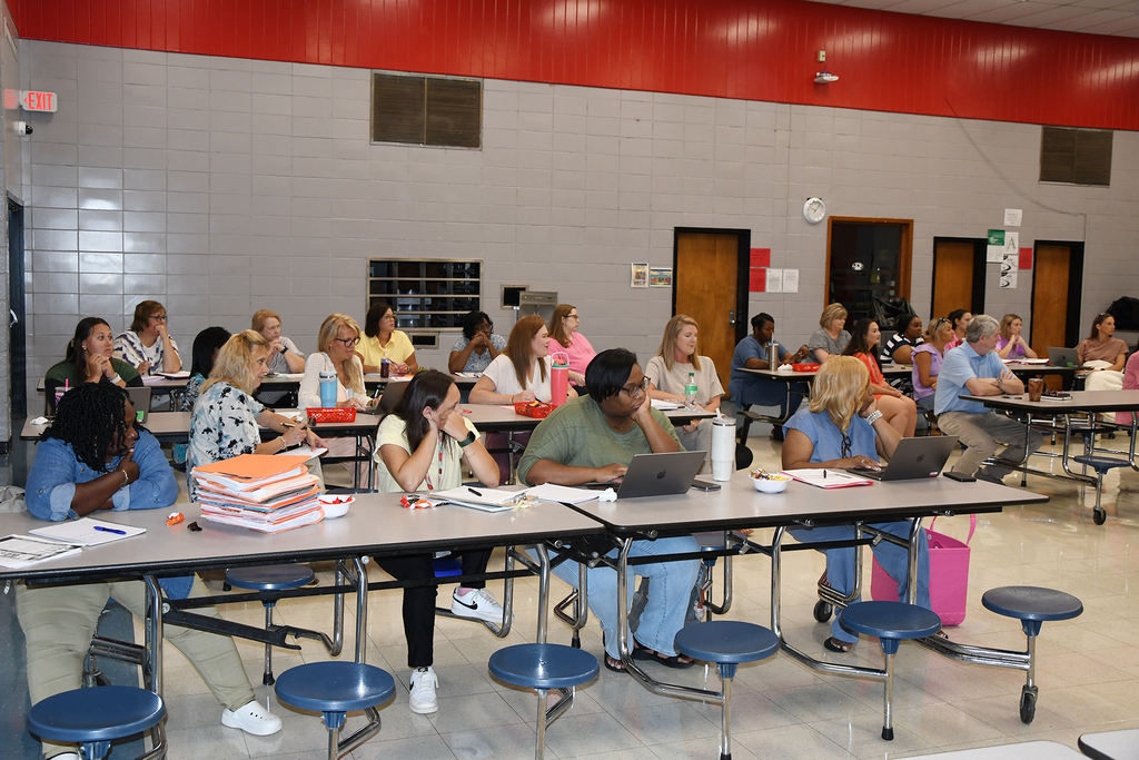 People seated at tables with laptops and papers, in a room with red and gray walls.