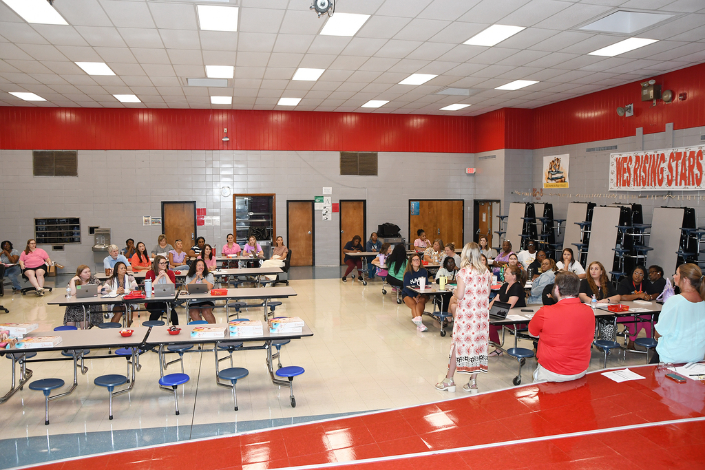 Room with red walls and white ceiling. People seated at tables. A banner reads "Welcoming Stars".