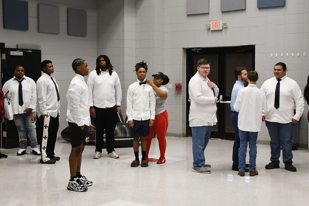 A group of people in white shirts and ties stand in a room with white floors and gray walls.
