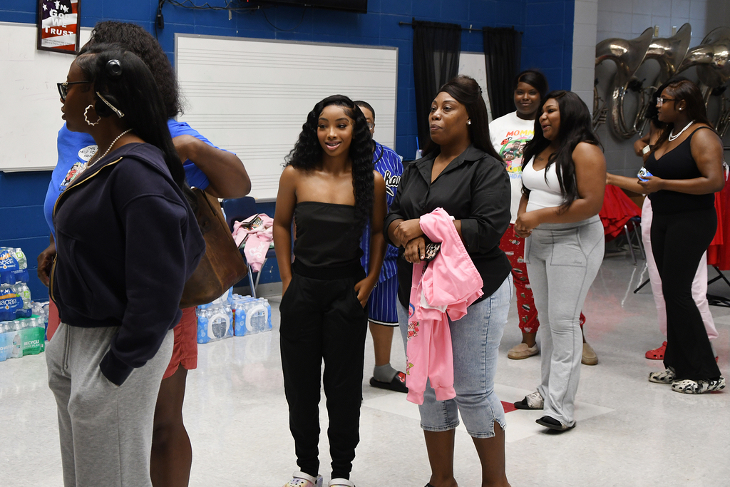A group of women in various outfits stand in a room with a blue wall and white ceiling.