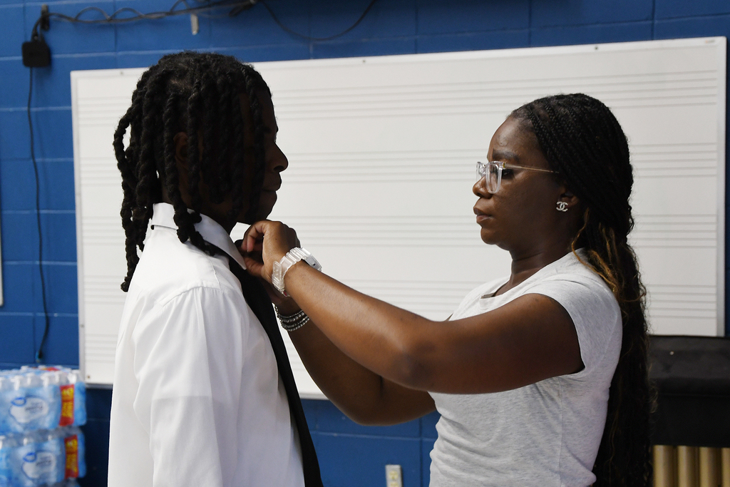 A woman adjusts the tie of a man in a white shirt, standing against a blue wall.