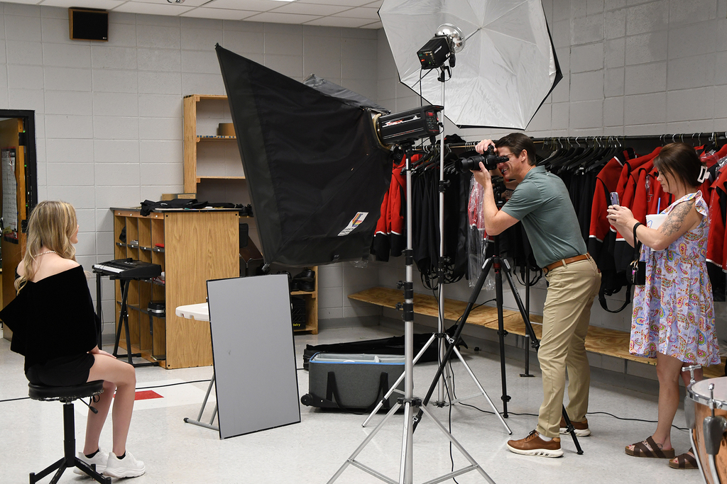 Studio setup with a person taking a photo of a seated woman, using a camera on a tripod and a black light umbrella.