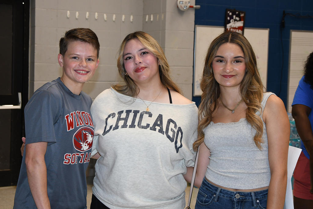 Three teens standing together, smiling at camera. The girl on left wears a Chicago shirt, middle wears a white shirt.