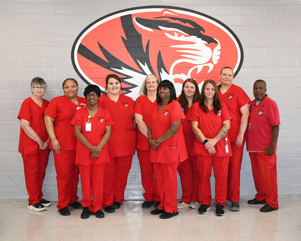 A group of staff in red uniforms pose together in front of a wall with a large tiger logo.