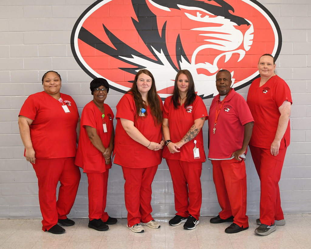 Six people in red scrubs standing in front of a wall with a tiger logo.