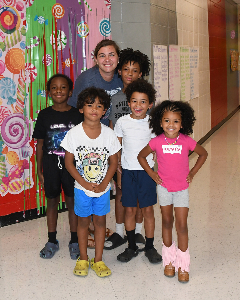 Five children and a woman pose in a colorful hallway with candy-themed wall decorations.