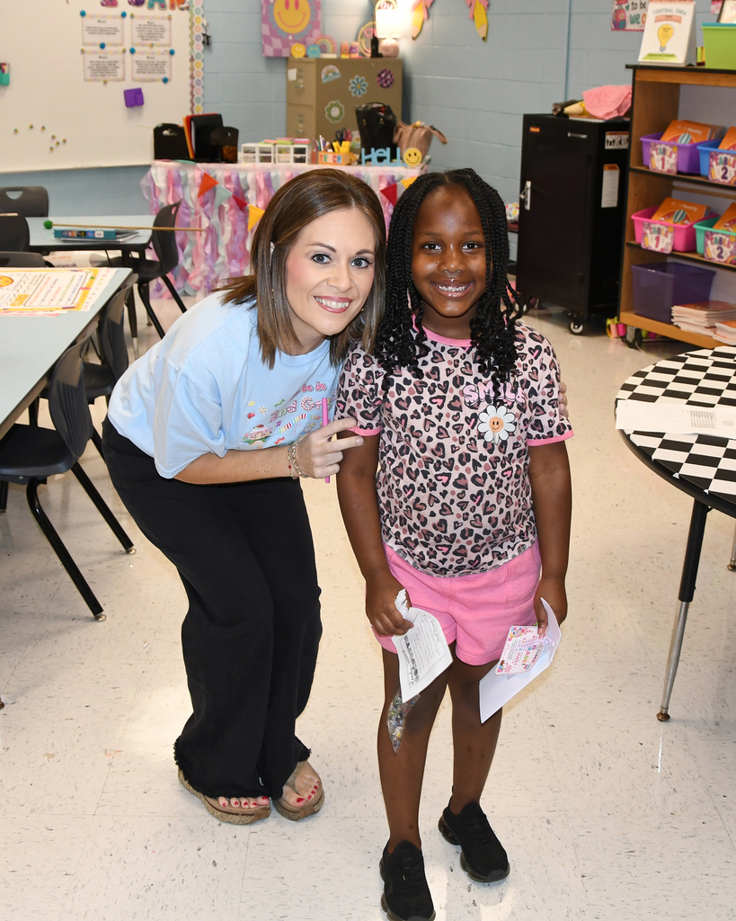 Woman in a light blue shirt standing next to a child in a leopard print shirt and pink shorts holding papers.
