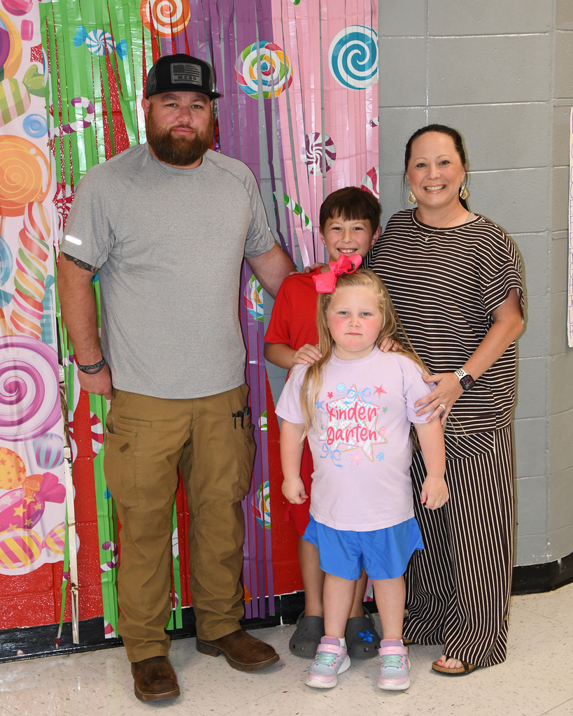 A family stands together in a room with candy-themed wall decorations, smiling for a photo.