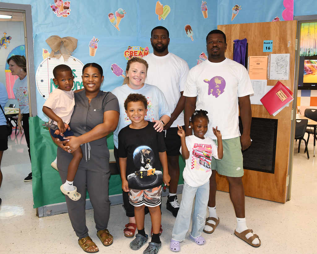 A family of seven stands close together in front of a wall decorated with ice cream.