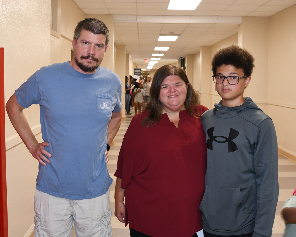 A man, a woman, and a boy stand together in a hallway, smiling and facing the camera.