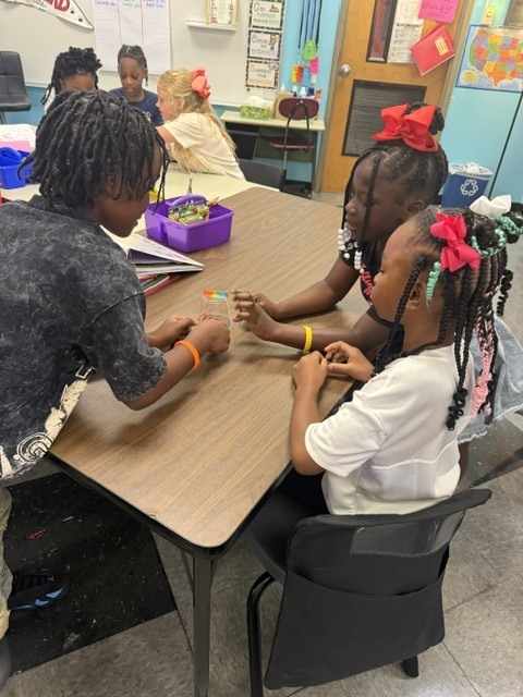 A classroom with children seated at a table. One child holds a stick while others look on.