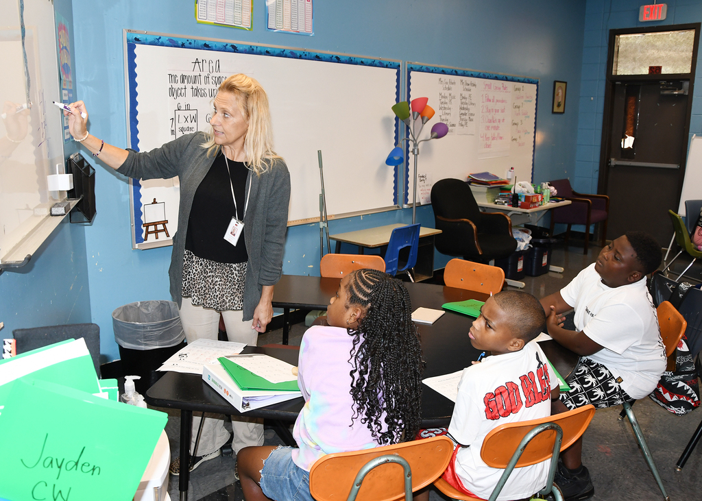 A woman teaching in a classroom. Three students seated at a table in front of her.