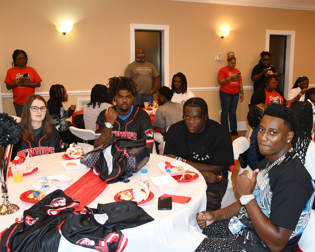 A group of people gathered around a table at an event. Some are seated while others stand nearby.